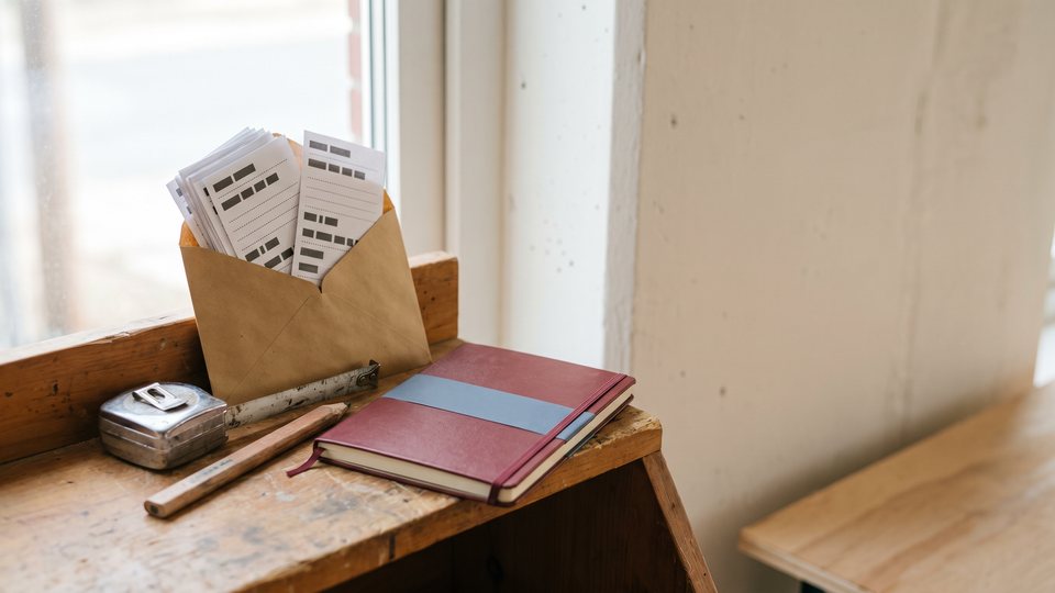 A kraft envelope of blank receipts beside a tape measure, a pencil and a red notebook on a tool bench